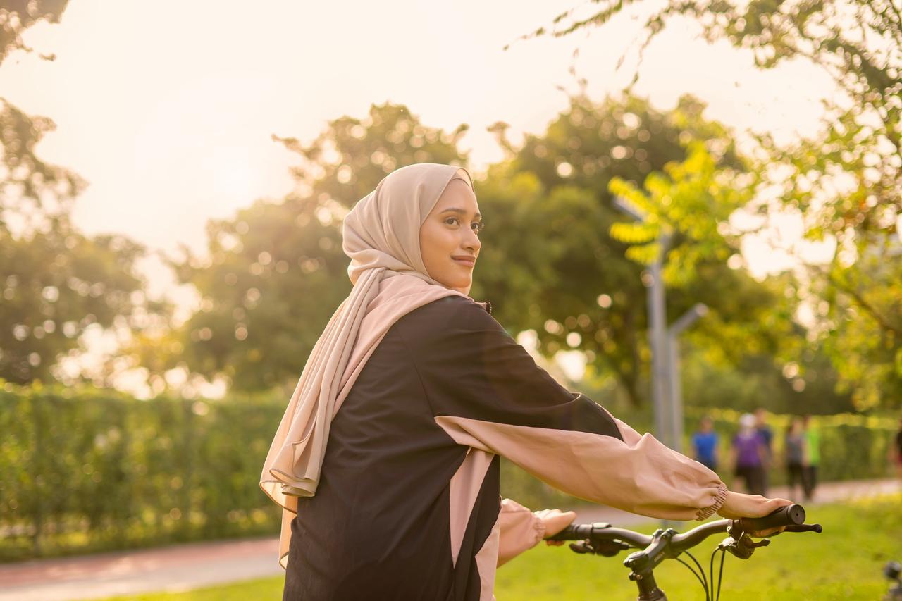 Woman wearing a hijab riding a bike at the park in the sunrise.jpg